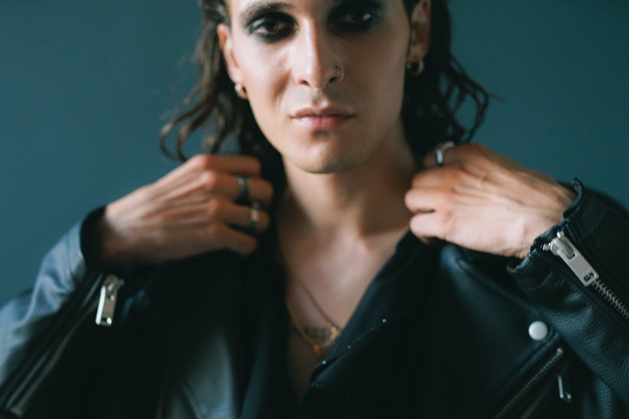 services-06 Portrait of a man in a black leather jacket showing edgy eye makeup, posing indoors.